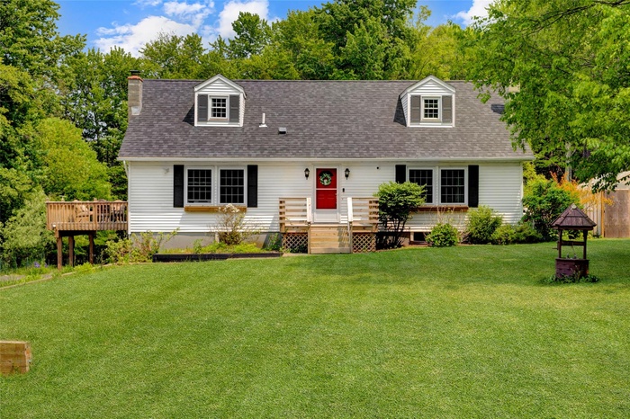 Cape cod home with a front yard, a chimney, a deck, and roof with shingles