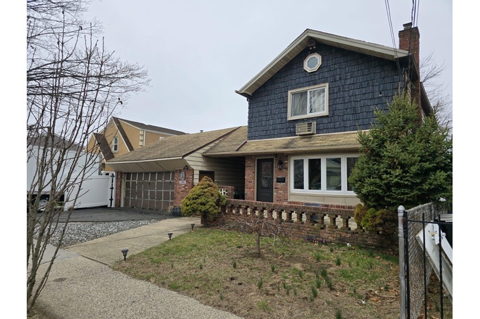 View of front of house with a chimney, brick siding, fence, an attached garage, and driveway