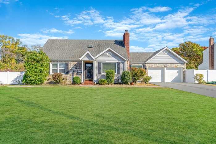 View of front facade with stone siding, a front lawn, fence, and concrete driveway