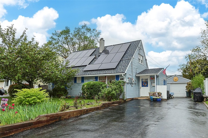 View of front facade featuring driveway, a shingled roof, roof mounted solar panels, a chimney, and a garage
