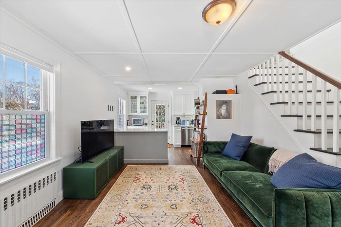 Living room with radiator heating unit, plenty of natural light, dark hardwood / wood-style floors, and ornamental molding