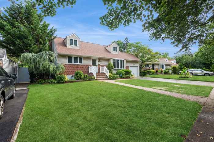 New england style home featuring a garage, brick siding, driveway, and a front lawn