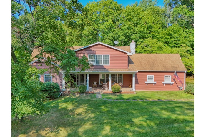 View of front of home featuring covered porch, a front lawn, a chimney, and a shingled roof