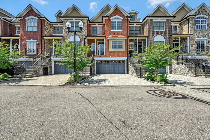 View of front facade featuring stairs, an attached garage, decorative driveway, and brick siding