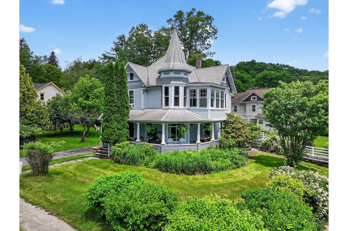 Victorian-style house featuring covered porch, a front yard, a shingled roof, and a chimney