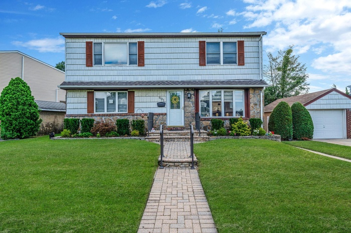 Traditional-style home with a front yard, stone siding, a detached garage, and an outbuilding
