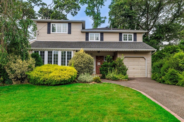 Traditional-style house featuring roof with shingles, asphalt driveway, a front lawn, and an attached garage