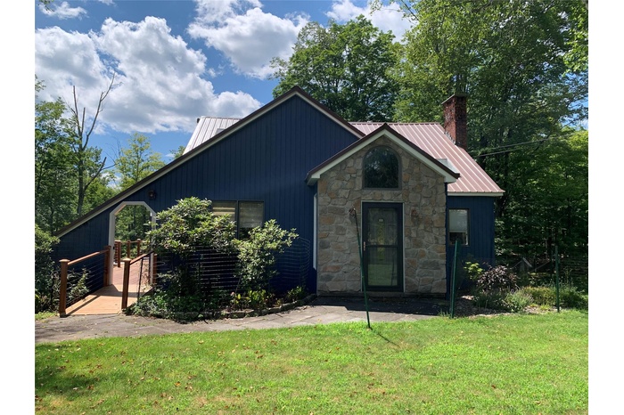 View of front of home featuring a metal roof, stone siding, a front yard, a deck, and a chimney