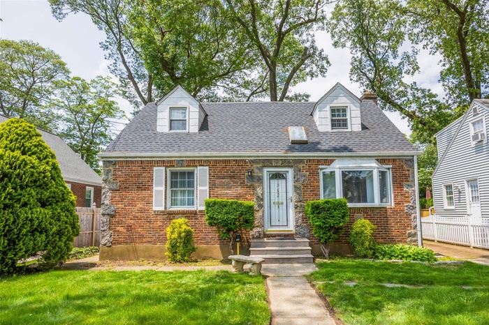 Cape cod home with brick siding and a shingled roof