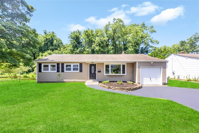 Ranch-style home featuring an attached garage, asphalt driveway, a front yard, and a chimney