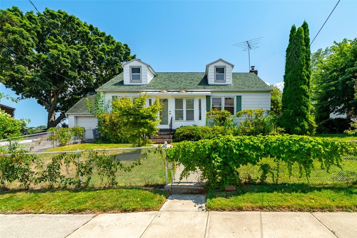 Cape cod home featuring a fenced front yard, a garage, a gate, and roof with shingles