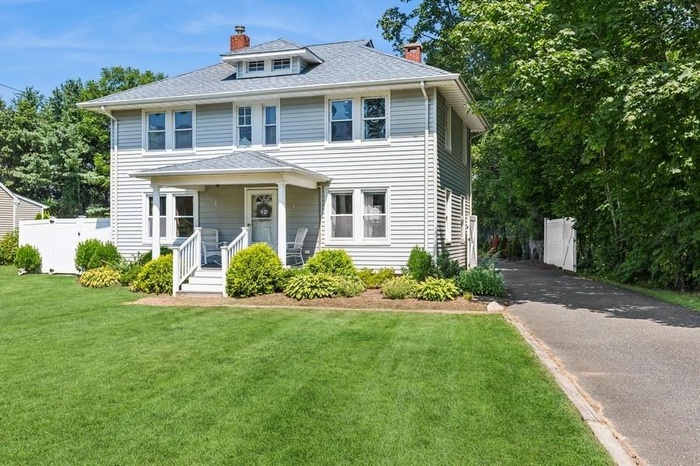 Traditional style home featuring a chimney, roof with shingles, asphalt driveway, and covered porch