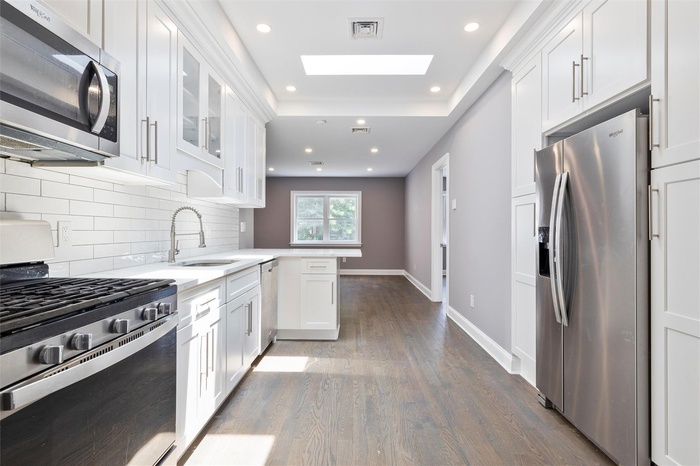 Kitchen featuring stainless steel appliances, a peninsula, backsplash, dark wood finished floors, and white cabinets