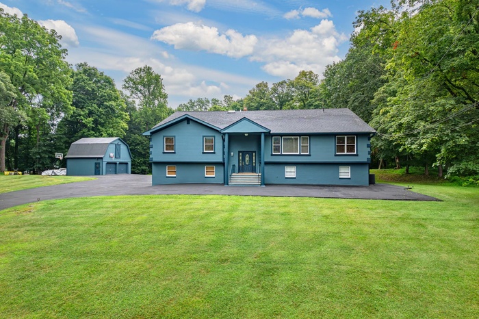 Raised ranch with an outbuilding, a front yard, driveway, view of wooded area, and a garage