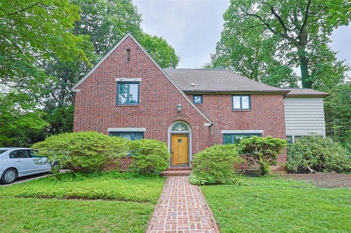 Tudor home with brick siding, a front lawn, and a shingled roof