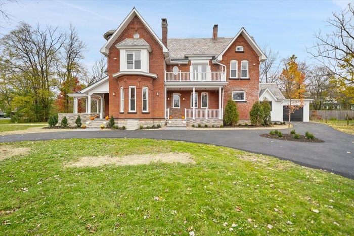 View of front of property with covered porch, brick siding, a chimney, and a balcony