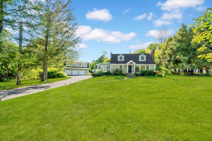 Cape cod house featuring concrete driveway, a front yard, a garage, and a chimney
