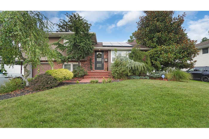 Tri-level home featuring a front lawn, solar panels, brick siding, a garage, and a shingled roof