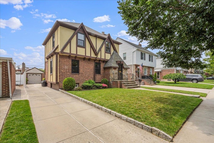 Tudor house featuring concrete driveway, an outbuilding, brick siding, stucco siding, and a front lawn