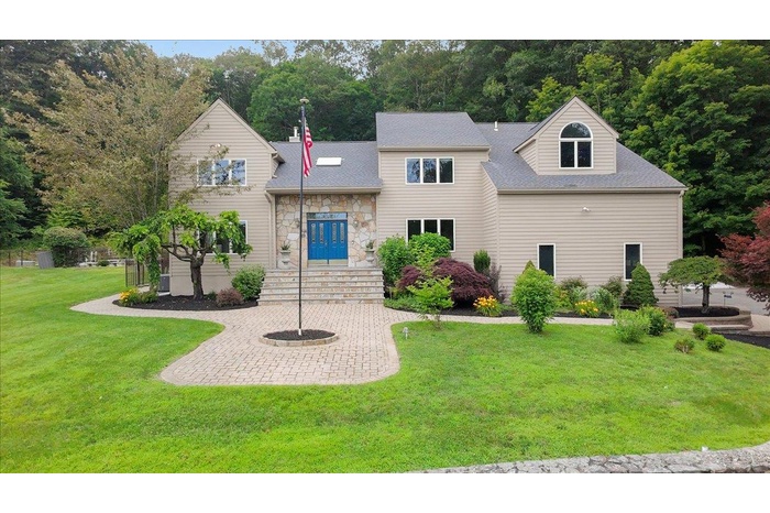 View of front of home featuring a front lawn, stone siding, and roof with shingles