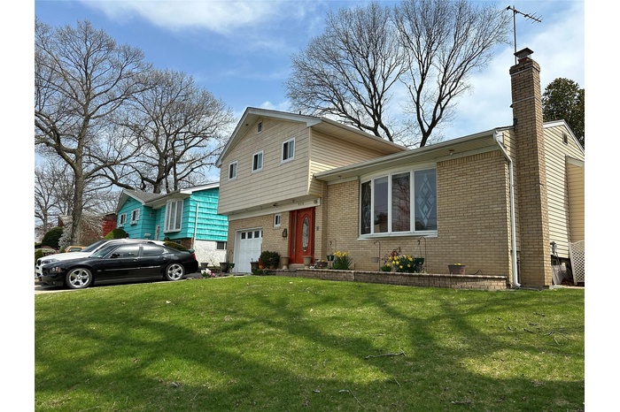 Tri-level home featuring a front lawn, brick siding, and a garage