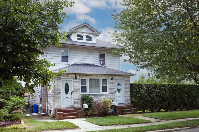 American foursquare style home featuring entry steps, stone siding, a shingled roof, and a front yard