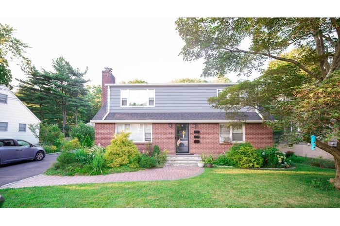 View of front of property featuring brick siding, a chimney, a front yard, and roof with shingles