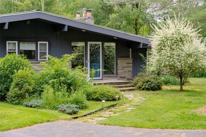 View of exterior entry featuring a chimney, stone siding, and a lawn