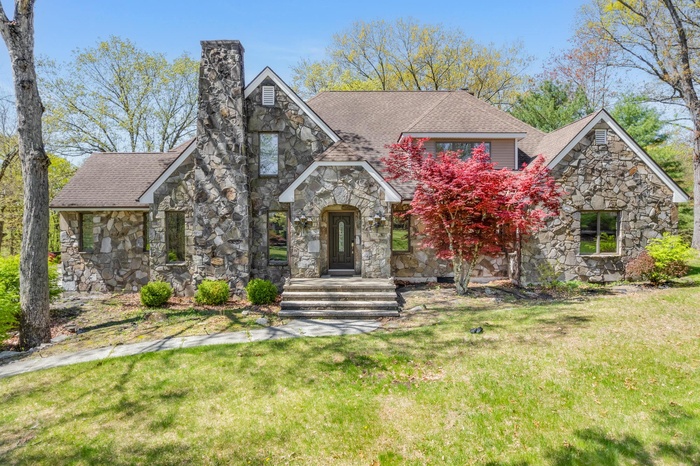 English style home featuring a chimney, a shingled roof, stone siding, and a front lawn