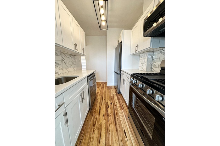 Kitchen featuring stainless steel appliances, white cabinetry, decorative backsplash, light wood-style flooring, and light stone counters