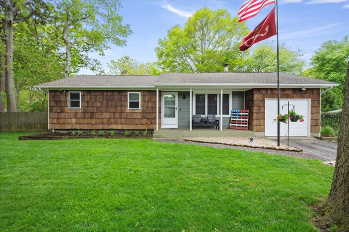 Ranch-style home featuring covered porch, a garage, roof with shingles, and asphalt driveway