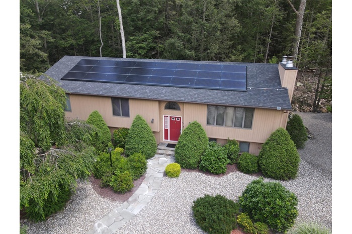 Raised ranch featuring roof with shingles, roof mounted solar panels, and a wooded view