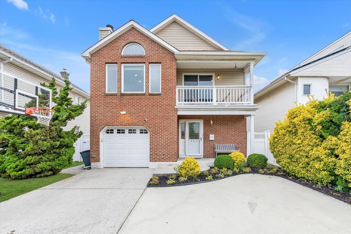 View of front of house with a balcony, brick siding, concrete driveway, an attached garage, and a chimney
