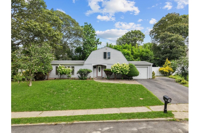 Colonial inspired home with a gambrel roof, driveway, a front yard, a garage, and view of wooded area