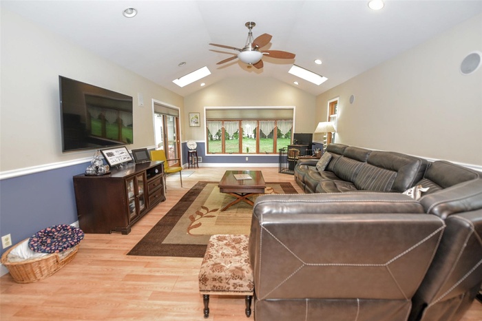 Living area featuring a skylight, light wood finished floors, ceiling fan, vaulted ceiling, and recessed lighting