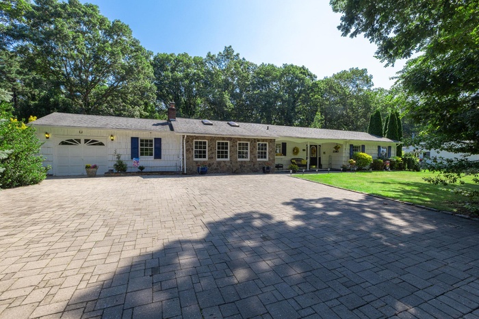 Ranch-style home featuring a chimney, a garage, a front lawn, driveway, and stone siding