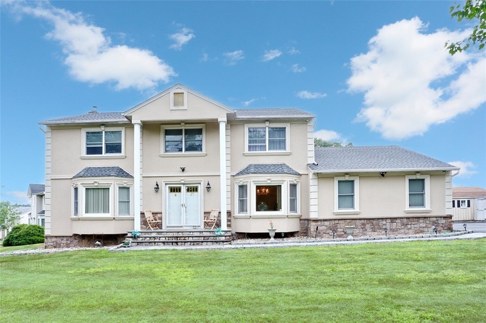 View of front of property featuring a shingled roof, stucco siding, a front lawn, and stone siding