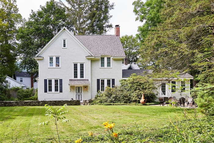 View of front facade featuring a shingled roof, a chimney, and a front lawn