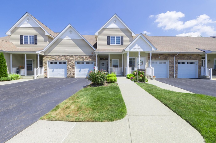 View of front of home featuring a porch, stone siding, asphalt driveway, a shingled roof, and a front yard