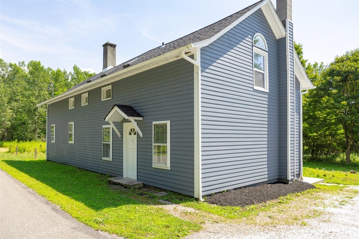 View of home's exterior featuring a chimney, a yard, and a shingled roof