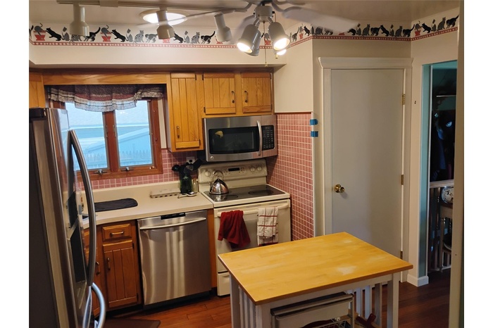 Kitchen featuring stainless steel appliances, ceiling fan, tile walls, dark wood-style flooring, and wainscoting