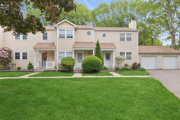 Townhome / multi-family property featuring a chimney, driveway, a front lawn, and a garage