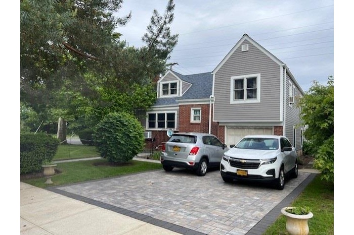 View of front facade featuring decorative driveway, brick siding, an attached garage, and a front lawn