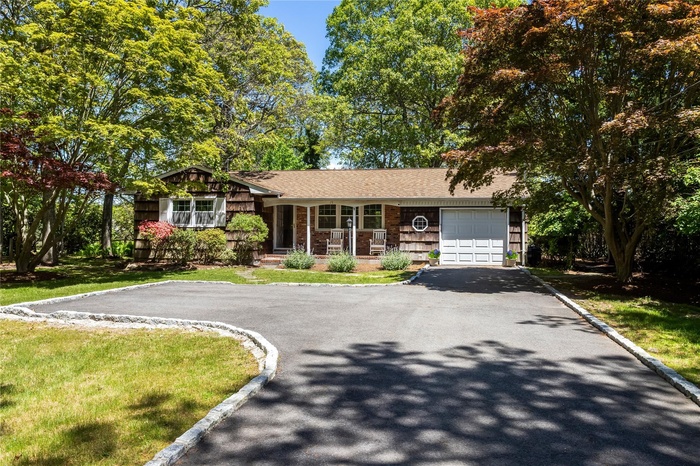 View of front of house featuring asphalt driveway, an attached garage, covered porch, roof with shingles, and a front yard