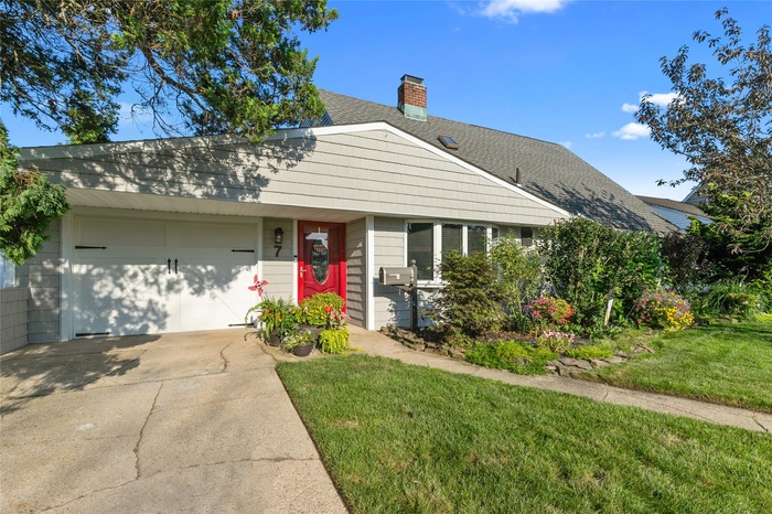 View of front facade featuring a shingled roof, a garage, driveway, a chimney, and a front yard