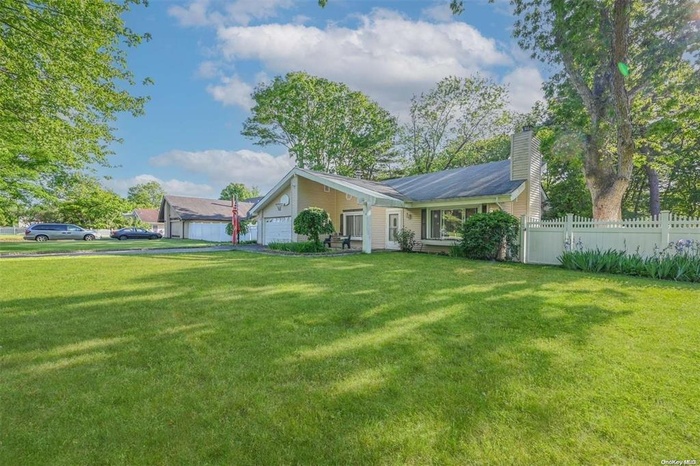 Rear view of property with aphalt driveway, fence, an attached garage, a chimney, and a yard