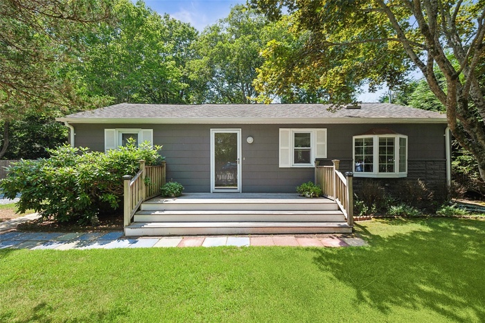 View of front of property with a front yard, a shingled roof, a deck, and stone siding