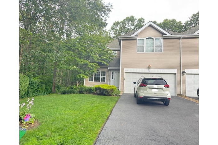 Traditional-style house featuring asphalt driveway, a front yard, an attached garage, and roof with shingles