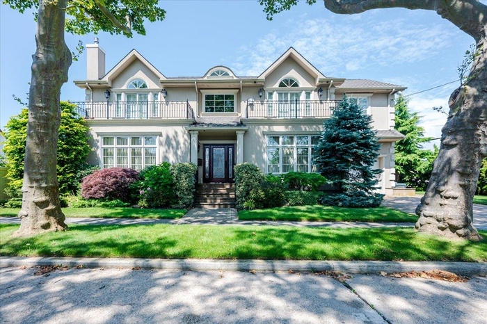 View of front of property with a balcony, stucco siding, a chimney, and a front lawn