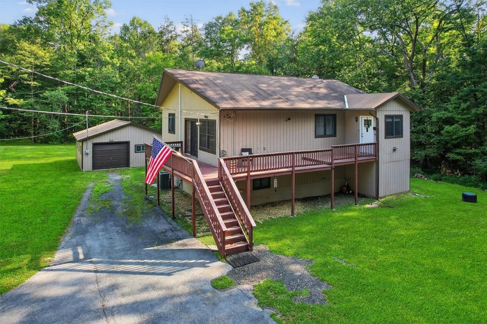 View of front of house with an outdoor structure, asphalt driveway, a detached garage, a shingled roof, and a wooden deck